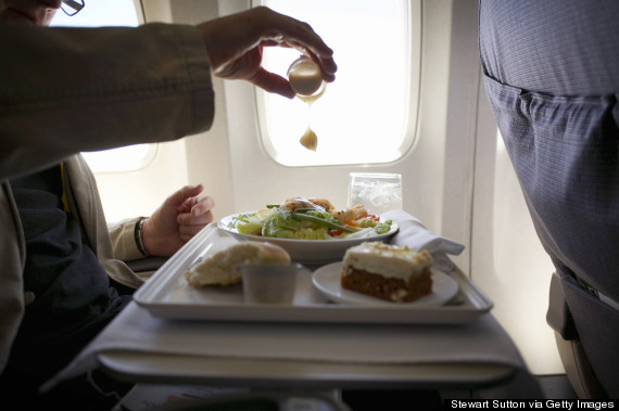 Mid adult man sitting at airplane, adding mustard to salad