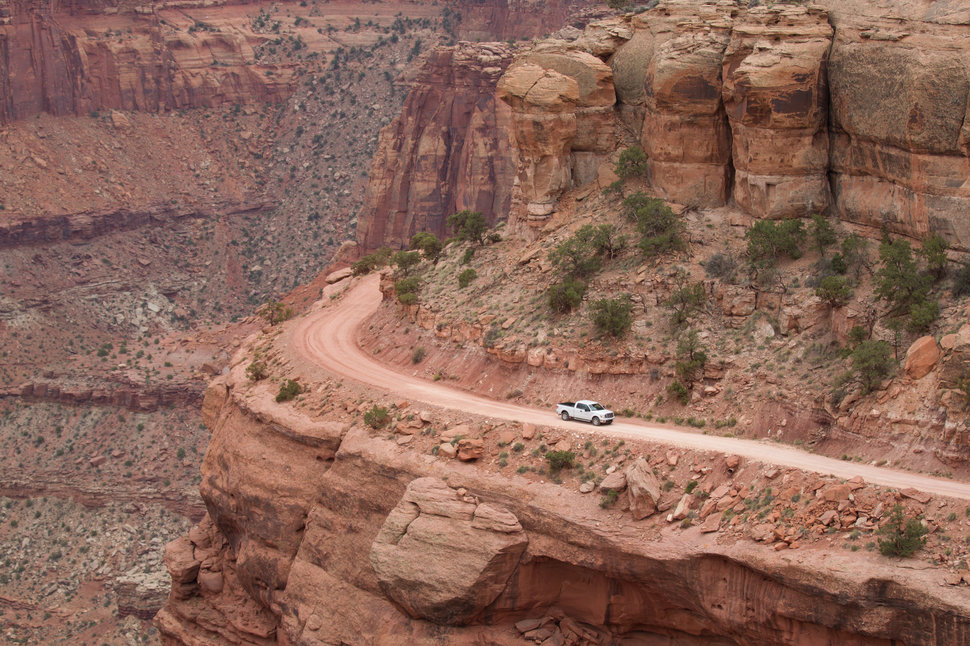 A truck drives along a dirt road on the edge of cliff in Canyonlands National park in Utah.