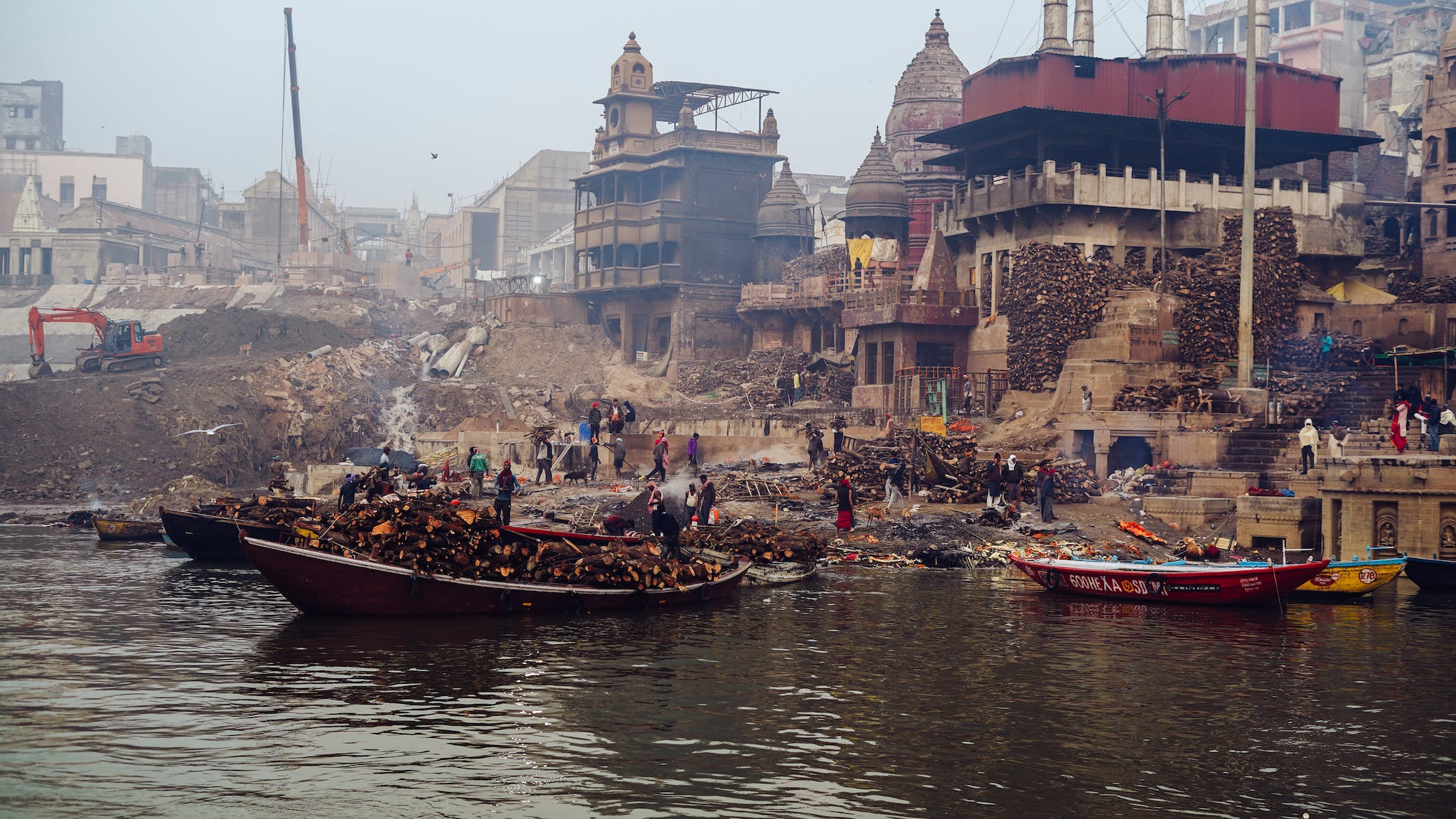 People Stacking Timber in Front of a Riverside Construction Site